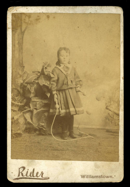 Young boy standing next to a plant holding a skipping rope