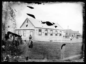 Glass plate negative image of a small weatherboard hall with the word 'welcome' written across the side wall