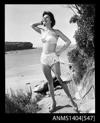 Photographic negative of a swimsuit model posing in a bikini on a small beach