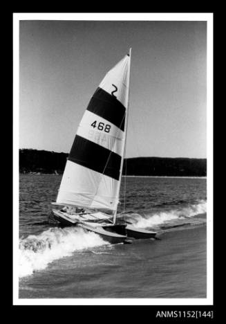 Print depicting starboard bow view of single sail catamaran just beaching