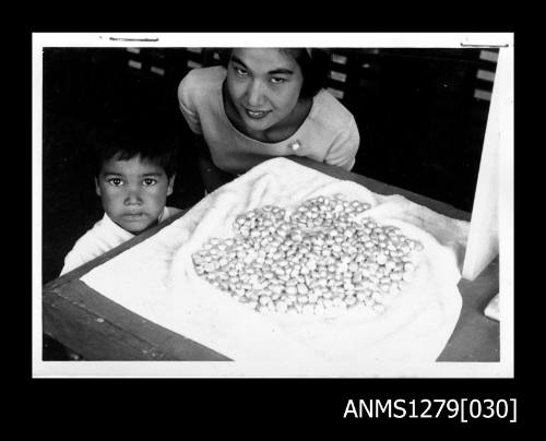 Yurie (or Yulie) George and her young son, with a large pile of half pearls (or mabe pearls) laid out on a towel