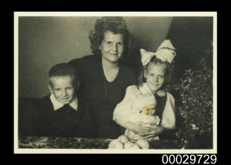A woman standing with a little boy and girl holding a doll