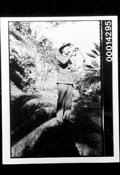 An Australian soldier plays a bugle in a garden
