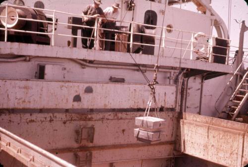 Slide depicting the lowering of a small boxes down hatch on ship